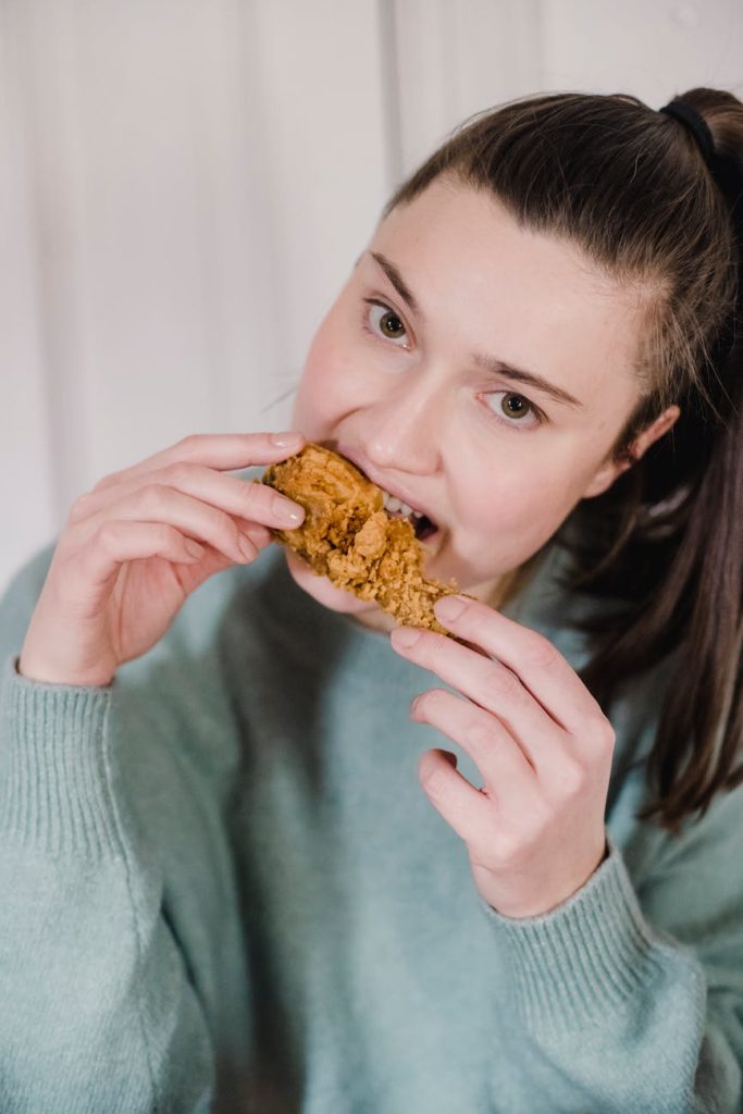 young woman eating tasty spicy fried chicken in breading